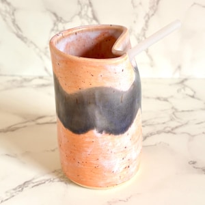 Puede incluir: Jarra de cer&aacute;mica hecha a mano con un dise&ntilde;o &uacute;nico. La jarra presenta un exterior color melocot&oacute;n con un patr&oacute;n de ondas gris oscuro y una pajita blanca. La jarra mide aproximadamente 15 cm de alto.