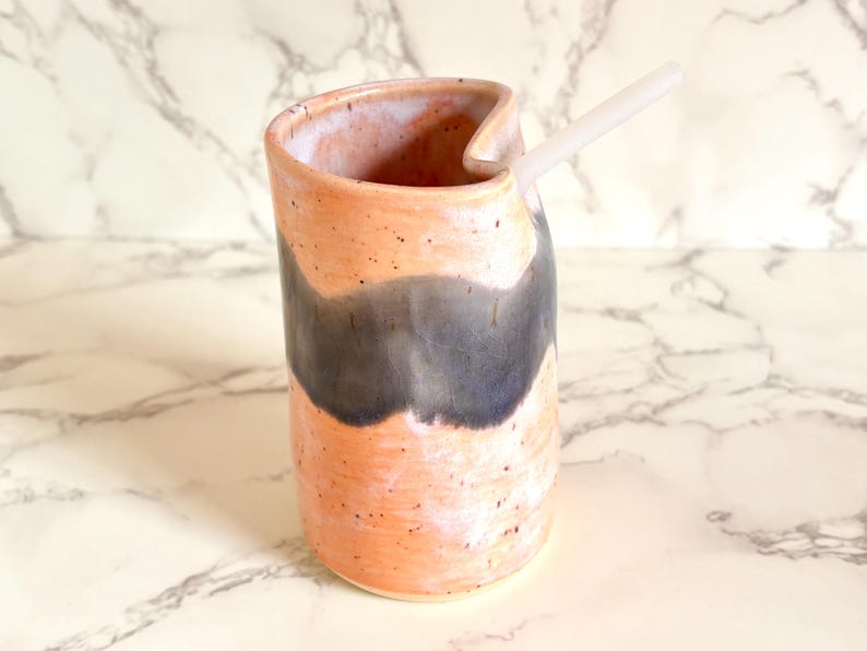 Puede incluir: Jarra de cer&aacute;mica hecha a mano con un dise&ntilde;o &uacute;nico. La jarra presenta un exterior color melocot&oacute;n con un patr&oacute;n de ondas gris oscuro y una pajita blanca. La jarra mide aproximadamente 15 cm de alto.