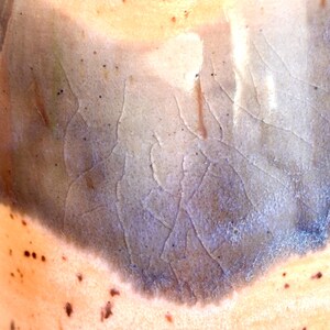 Puede incluir: Primer plano de un recipiente de cer&aacute;mica con una superficie texturizada. El esmalte transita de un melocot&oacute;n claro a un azul-gris oscuro, con patrones de craquelado visibles. Peque&ntilde;os puntos oscuros est&aacute;n dispersos por la superficie.