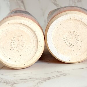 Puede incluir: Dos jarras de cer&aacute;mica con una base moteada de color blanquecino y una banda de color rosa, gris y negro. Se ven los fondos, cada uno estampado con un dise&ntilde;o circular y la palabra "MADE". Cer&aacute;mica.