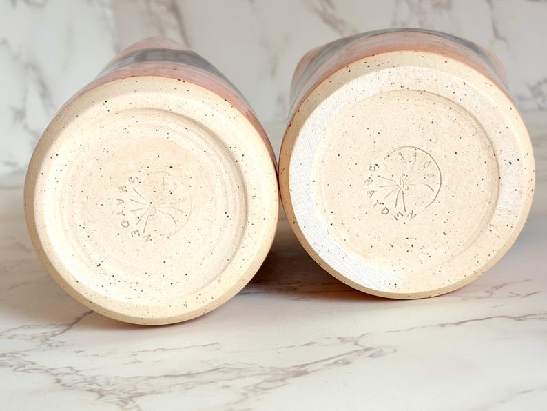 Puede incluir: Dos jarras de cer&aacute;mica con una base moteada de color blanquecino y una banda de color rosa, gris y negro. Se ven los fondos, cada uno estampado con un dise&ntilde;o circular y la palabra "MADE". Cer&aacute;mica.