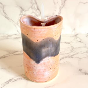Puede incluir: Un vaso de cer&aacute;mica hecho a mano con un dise&ntilde;o &uacute;nico. El vaso presenta una base de color melocot&oacute;n con un patr&oacute;n de ondas gris oscuro. Una pajita blanca est&aacute; insertada en la parte superior. El vaso est&aacute; salpicado de peque&ntilde;os puntos negros.