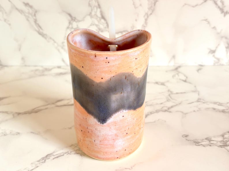 Puede incluir: Un vaso de cer&aacute;mica hecho a mano con un dise&ntilde;o &uacute;nico. El vaso presenta una base de color melocot&oacute;n con un patr&oacute;n de ondas gris oscuro. Una pajita blanca est&aacute; insertada en la parte superior. El vaso est&aacute; salpicado de peque&ntilde;os puntos negros.