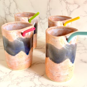 Puede incluir: Cuatro vasos de cer&aacute;mica hechos a mano con pajitas de silicona de colores. Los vasos tienen un dise&ntilde;o moteado en melocot&oacute;n y azul. Cada vaso tiene una pajita de diferente color: rosa, verde, amarillo y turquesa.