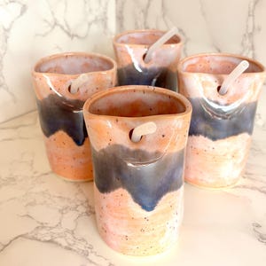 Puede incluir: Cuatro vasos de cer&aacute;mica hechos a mano con un dise&ntilde;o &uacute;nico. Las tazas presentan una combinaci&oacute;n de colores melocot&oacute;n y azul con una textura moteada. Cada vaso tiene un agujero cerca de la parte superior e incluye una pajita blanca.