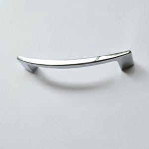 May include: A polished chrome cabinet handle with a sleek, gently curved arch design. The hardware features a smooth, reflective metallic finish and two angled mounting points at each end, providing a clean and modern look for furniture.