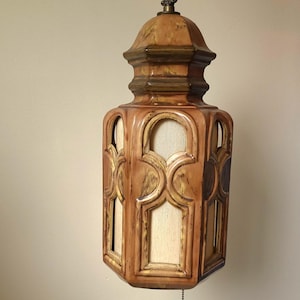 May include: Vintage hanging light fixture with a warm, earthy color palette. The fixture features a decorative, geometric design with a light-colored interior. The light hangs from a chain and has a pull chain for operation.