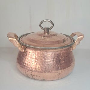 May include: A hammered copper pot with a lid and two handles. The pot has a silver rim and a silver knob on the lid.