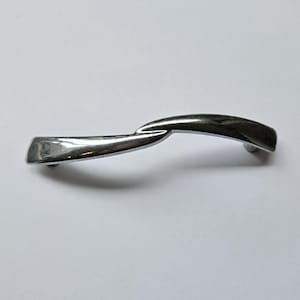 May include: A polished chrome cabinet pull with a smooth, undulating S-shaped design. The metal handle features a reflective, silver-toned finish with tapered ends and a curved profile that creates a continuous, flowing form across its length.