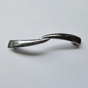 May include: A polished chrome cabinet handle featuring a smooth, undulating wave-like shape. The metal hardware has a reflective, silver-toned finish with a curved, elongated design that tapers slightly at both ends, creating a sleek, continuous form.