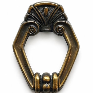 May include: Antique brass-toned drawer pull with an Art Deco design. The pull features a decorative top with a fan-like pattern and scrolled sides. The handle has an octagonal shape with a series of vertical bars at the base.