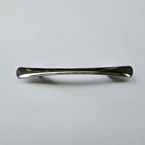 May include: A polished silver-toned metal cabinet pull with a smooth, elongated, and slightly curved design. The handle features a slender centre that gradually widens towards the rounded, flared ends, creating a sleek and uniform metallic finish.