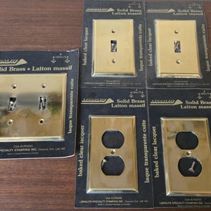 Peut inclure: Cinq plaques murales Libralite en laiton massif avec finition laquée transparente cuite, comprenant une plaque pour double interrupteur, deux pour interrupteur simple et deux pour prise double, dans leur emballage noir d'origine avec vis.