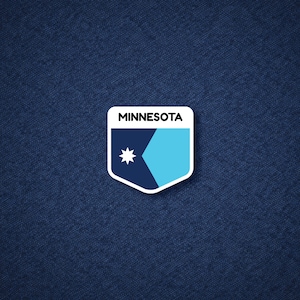 May include: A white-bordered sticker featuring the word "MINNESOTA" above a shield design. The shield is divided into sections of navy blue and light blue, with a white star in the navy blue section. The sticker is on a textured navy blue background.