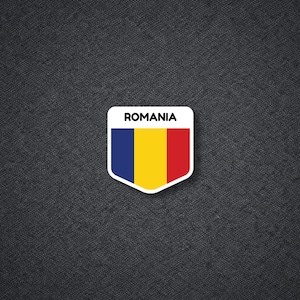 May include: A white, shield-shaped sticker with the word "ROMANIA" in black text at the top. The sticker features the Romanian flag: a vertical tricolor of blue, yellow, and red.