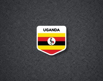 May include: A shield-shaped sticker featuring the national flag of Uganda with horizontal stripes of black, yellow, and red. The word UGANDA is printed in black at the top, and a circular emblem of a grey crowned crane is centered on the flag.