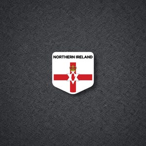 May include: A white, shield-shaped sticker featuring the flag of Northern Ireland. The flag has a red cross, a six-pointed star, and a crown. The text "NORTHERN IRELAND" is printed at the top of the sticker.