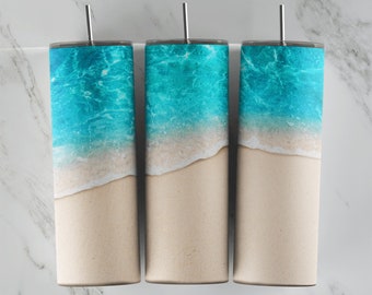 Könnte beinhalten: Drei Edelstahlbecher mit Strandmotiv. Die Becher zeigen ein blaues Meer mit weißen Wellen, die an einem Sandstrand brechen.