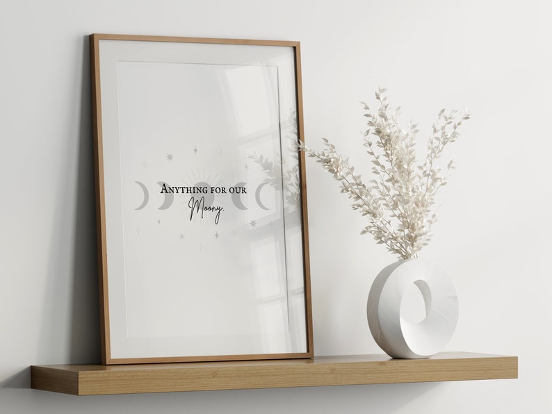 May include: A framed print with the text "Anything for our Moon" and a crescent moon design in gray. The print is on a wooden shelf with a white vase and dried white flowers.