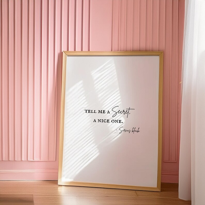 May include: A framed print with a white background and black text that reads "Tell me a secret. A nice one. - Sirius Black". The frame is light wood and the print is hanging on a pink wall.