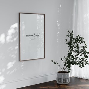 May include: A framed print with the text "You were beautiful" and the artist's name "Soren Hood" in a white room with a potted plant.