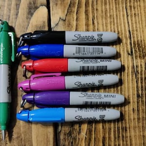 May include: A set of eight Sharpie brand permanent markers in various colors, including black, blue, red, pink, purple, and light blue. The markers are all mini size and have a silver cap with the Sharpie logo.