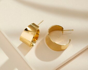 May include: A pair of gold hoop earrings with a wide, flat band. The earrings are simple and elegant.