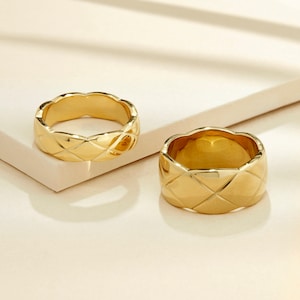 May include: Two gold-toned rings with a quilted design. The rings are thick and have a rounded shape.