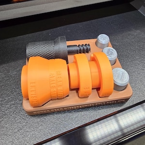Op de afbeelding: Een assortiment auto-onderdelen, waaronder oranje en zwarte componenten, is gerangschikt op een bruine tray. De oranje onderdelen zijn voorzien van de tekst "REAR DIFF AXLE SET" en "LEVISION". Er zijn ook verschillende zilverkleurige, ronde stukken aanwezig.