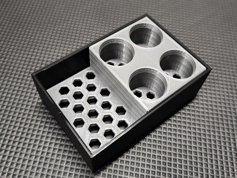Peut inclure: Un organisateur bicolore avec un plateau ext&eacute;rieur noir et un insert argent&eacute;. L'insert pr&eacute;sente un motif en nid d'abeille et quatre compartiments circulaires. L'organisateur est con&ccedil;u pour contenir de petits objets.