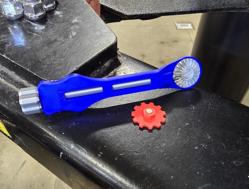 May include: A blue and silver tool with a red gear. The tool has a handle and a gear on one end. The gear is designed to fit into a larger gear.