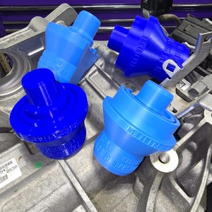 以下が含まれることがあります： さまざまな青色の4つの青い自動車部品が、銀色のエンジンコンポーネントに配置されています。部品は、フレアベースと中央の隆起部分を備えた円筒形をしています。テキストは部品の側面に表示されます。