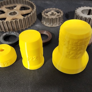 Op de afbeelding: Drie gele plastic gereedschappen voor het timen van de motor met het nummer 22 erop gedrukt. De gereedschappen liggen op een zwart oppervlak.