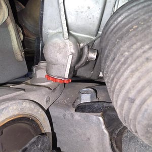 May include: Close-up of a car engine component with a red rubber gasket. The component is made of metal and has a silver finish. The component is attached to a black rubber hose.