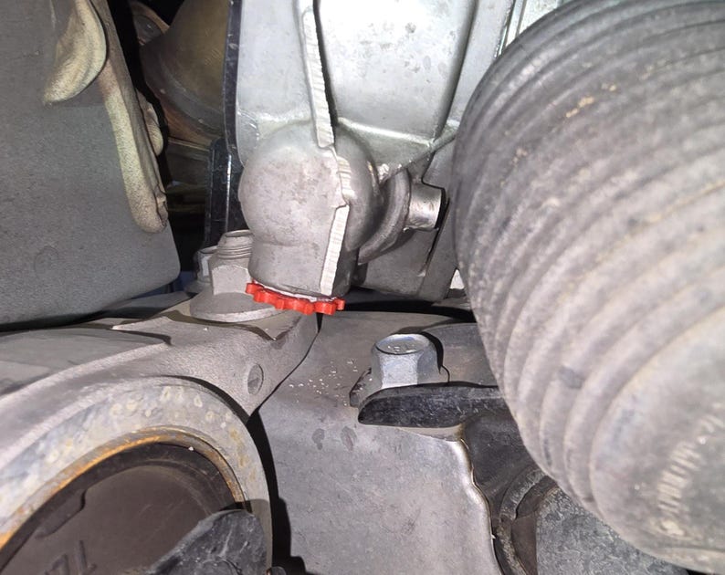 May include: Close-up of a car engine component with a red rubber gasket. The component is made of metal and has a silver finish. The component is attached to a black rubber hose.
