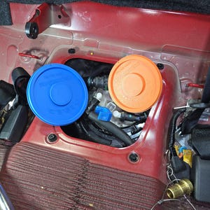 May include: A close-up of a car's undercarriage, showing two round fuel filter caps, one blue and one orange. The caps are labeled with the text "Fuel Filter".