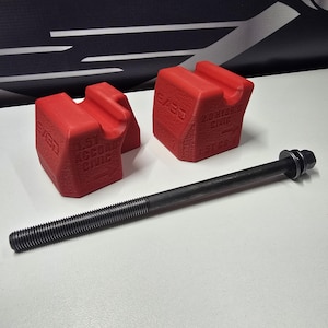 May include: Two red, textured, 3D-printed automotive support blocks featuring molded text including 1.5T ACCORD CIVIC and 2.0 HYBRID CIVIC 1.5T CR-V, accompanied by a long, slender, black metal bolt with a threaded shaft and a hexagonal head.
