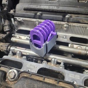 May include: A close-up of a purple and gray engine part with a series of circular openings. The part is sitting on top of a car engine.