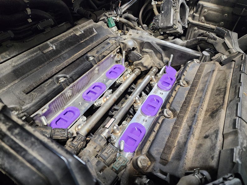 May include: Close-up of a car engine with purple intake manifold spacers. The spacers are installed on the intake manifold and are connected to the fuel injectors.