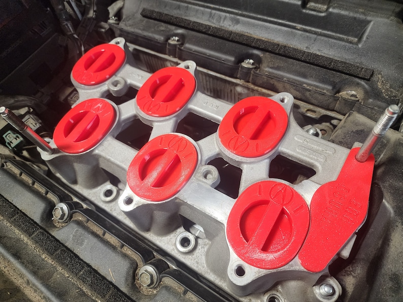 K&ouml;nnte beinhalten: Nahaufnahme eines Automotors mit sechs roten Ansaugkr&uuml;mmerabdeckungen. Die Abdeckungen haben ein erhabenes "100"-Logo.
