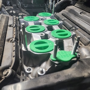 K&ouml;nnte beinhalten: Nahaufnahme eines Automotors mit gr&uuml;nen Ventildeckeln. Die Deckel haben einen schwarzen Streifen in der Mitte und der Text "EGR" ist auf einem der Deckel sichtbar.