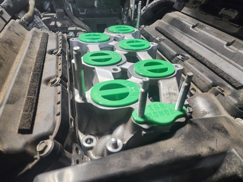 K&ouml;nnte beinhalten: Nahaufnahme eines Automotors mit gr&uuml;nen Ventildeckeln. Die Deckel haben einen schwarzen Streifen in der Mitte und der Text "EGR" ist auf einem der Deckel sichtbar.