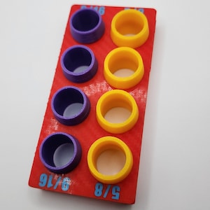 May include: A red plastic tool with purple and yellow rings. The tool is labelled with the fractions 5/8, 9/16, and 5/16.
