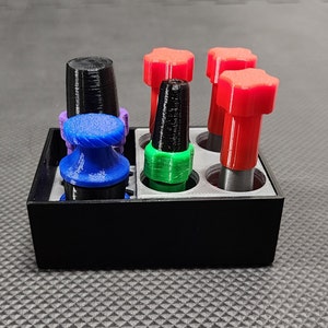 Peut inclure: Un organisateur rectangulaire noir contient plusieurs objets color&eacute;s imprim&eacute;s en 3D. Ceux-ci comprennent un objet bleu en forme de champignon, une pi&egrave;ce cylindrique noire et des objets rouges en forme d'&eacute;toile. L'organisateur est sur une surface textur&eacute;e.