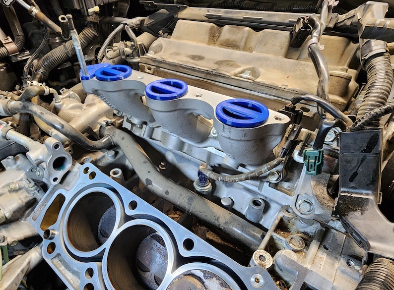 May include: Close-up of a car engine with a silver intake manifold and blue intake manifold covers. The engine is dirty and has a lot of wires and hoses.