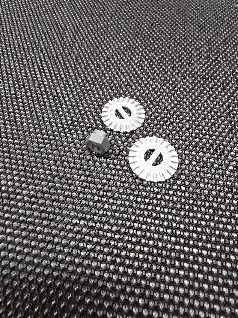 May include: Two silver cookie cutters with a decorative design and a silver nut on a black textured surface.