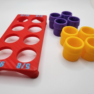 May include: A red plastic organiser with nine circular compartments for storing small items. The organiser has the text "5/8" and "6/16" printed on it. There are also six colourful plastic rings, four yellow and two purple, in the image.