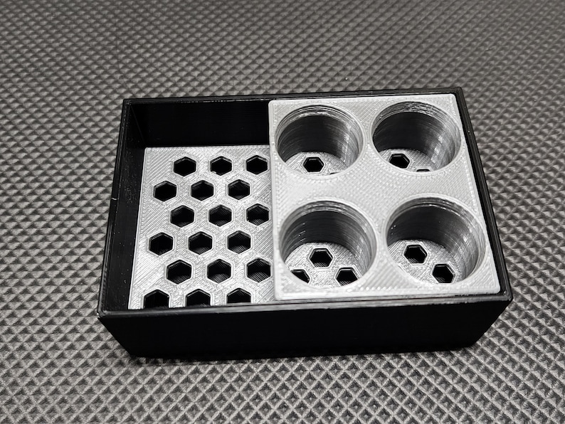 Peut inclure: Un organisateur noir et gris imprim&eacute; en 3D avec un motif en nid d'abeille et quatre compartiments circulaires. L'organisateur est con&ccedil;u pour contenir de petits objets, avec une surface textur&eacute;e.