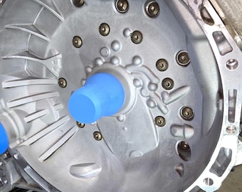 Pode incluir: Um close-up de uma caixa de transmissão de metal prateado com vários parafusos e uma tampa de plástico azul. A caixa está montada em um suporte de metal preto.