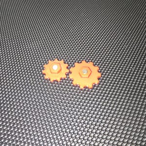 May include: Two orange plastic gears with a silver metal pin in the center of each gear.